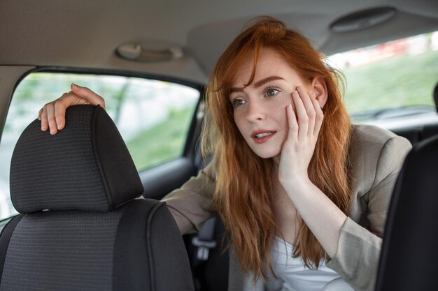 Bange vrouw die hand op het hoofd houdt tijdens het rijden in de auto op een wazige voorgrond