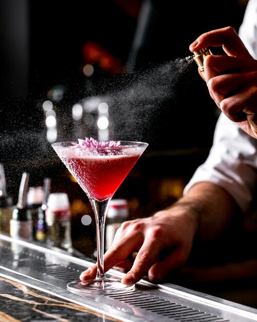 Bar tender sprays op cocktailglas gegarneerd met bloem