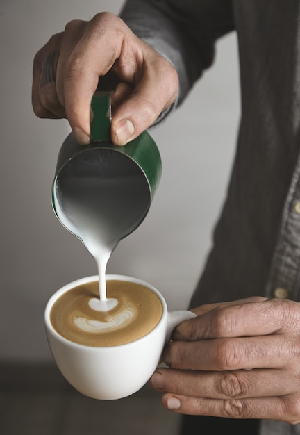 Barista bereidt cappuccino in lege witte kop voor en morst melkschuim in hartvorm. Koffie winkel.