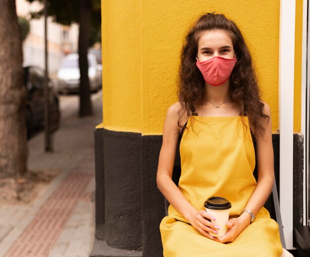 Barista draagt een gezichtsmasker terwijl hij buiten een kopje koffie houdt