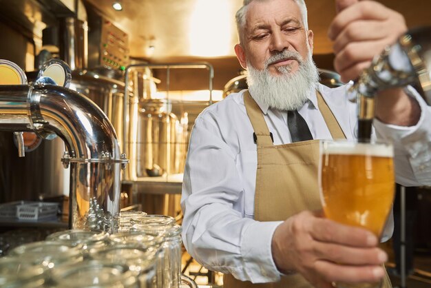 Barman in bruine schort die vers bier met schuim giet