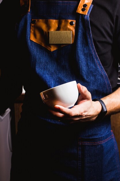 Barman met denim schort houdt een kopje vast