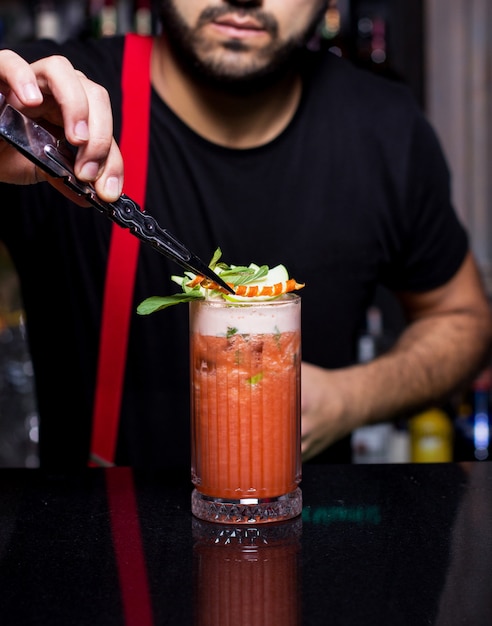 Barman plaatst sinaasappelschil over een glas sinaasappel- en appelcocktail