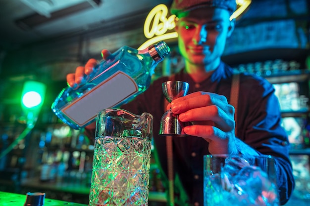 Barman voltooit de bereiding van een alcoholische cocktail met shaker in veelkleurig neonlicht