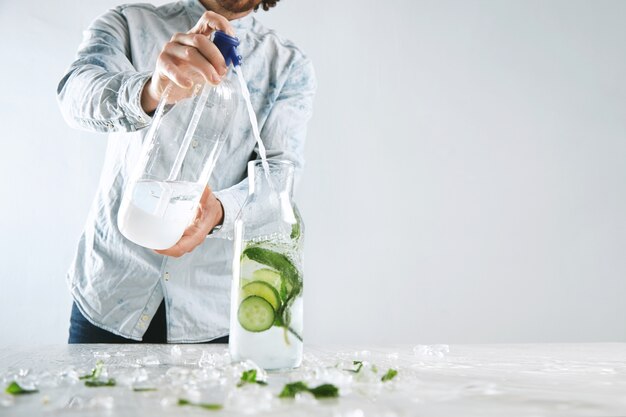 Bartender giet bruisend water in een vintage fles met ijs, komkommer en munt uit de sifon om een koude zomer gezonde drank te maken zoals mojito zonder alcohol