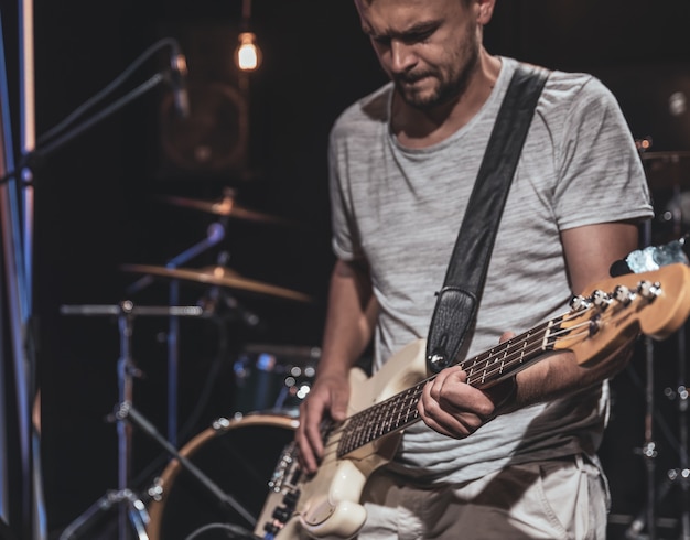 Basgitarist speelt de basgitaar in een donkere kamer op een onscherpe achtergrond.