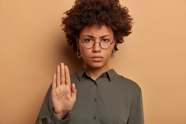 Gratis foto bazig ernstig uitziende vrouw kijkt strikt naar de camera, strekt de handpalm uit, drukt taboe of verbod uit, fronst het gezicht