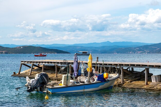 Beached metalen gemotoriseerde gekleurde boot op een pier aan de Egeïsche zee kosten, heuvels en een stad in Ouranoupolis, Griekenland