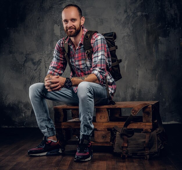 Bebaarde getatoeëerde backpacker man poseren in een studio op grijze achtergrond.