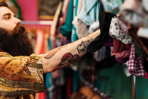 Bebaarde jonge man aan het shirt opknoping op het spoor in de kledingwinkel