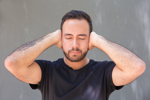 Gratis foto bebaarde jonge man sluitende oren met handen