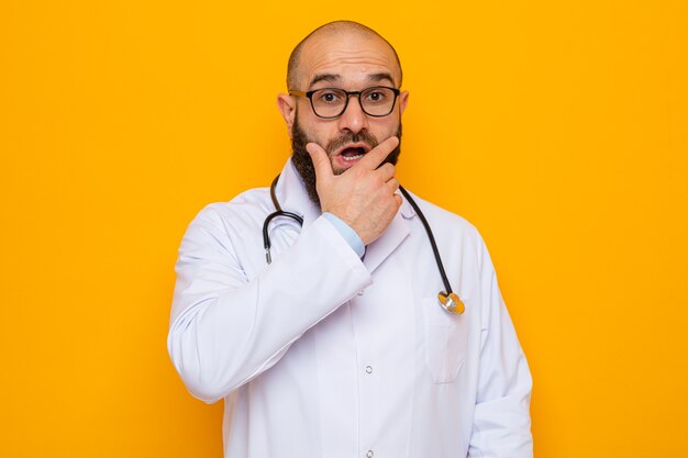 Bebaarde man arts in witte jas met stethoscoop om de nek met een bril die er verbaasd en verrast uitziet