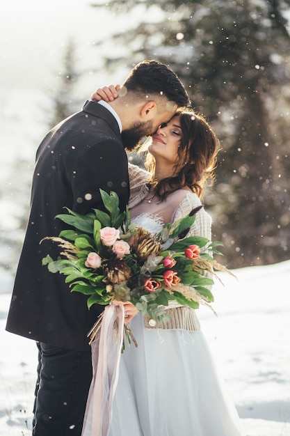 Bebaarde man en zijn mooie bruid poseren in de sneeuw in een magische winter bos