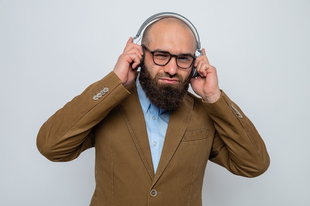 Bebaarde man in bruin pak met een bril met een koptelefoon die er glimlachend uitziet terwijl hij geniet van muziek