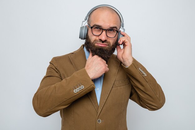 Bebaarde man in bruin pak met een bril met koptelefoon op zoek met peinzende uitdrukking