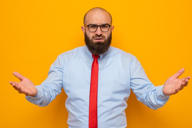 Bebaarde man in rode stropdas en blauw shirt met een bril die er verward uitziet en zijn armen naar de zijkanten spreidt