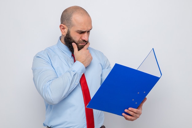 Bebaarde man in rode stropdas en blauw shirt met een kantoormap die er verbaasd naar kijkt terwijl hij op een witte achtergrond staat