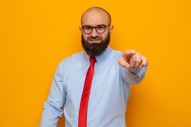 Bebaarde man in rode stropdas en shirt met een bril die er gelukkig uitziet en met de wijsvinger naar voren wijst