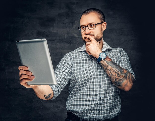 Bebaarde man in zonnebril houdt tablet-pc over grijze achtergrond.