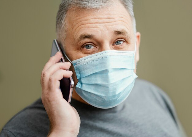 Bebaarde man met chirurgisch masker met behulp van telefoon