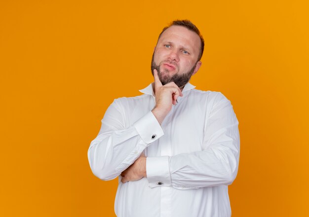 Bebaarde man met een wit overhemd opzij kijken verbaasd staande over oranje muur