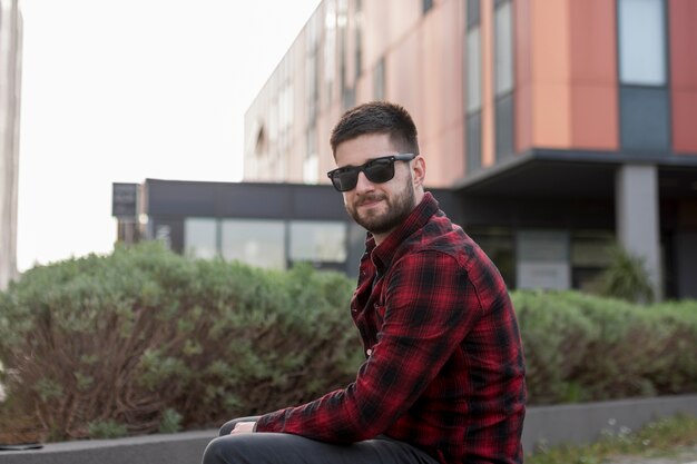 Bebaarde man met een zonnebril zitten en kijken naar de camera