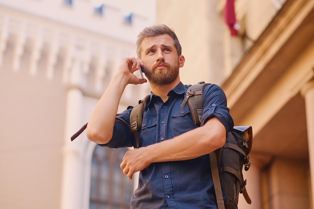 Bebaarde man met rugzak spreken via smartphone in een oude Europese stad.