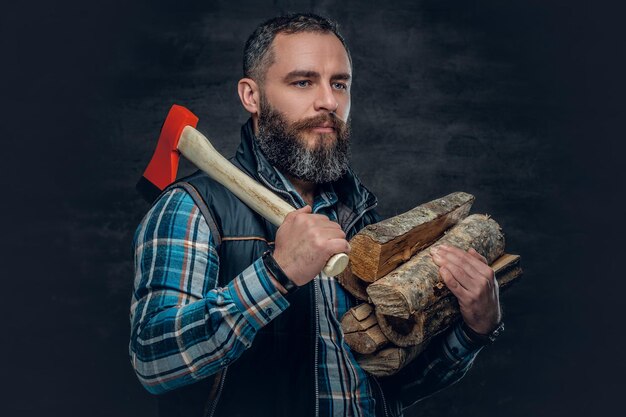 Bebaarde man van middelbare leeftijd houdt een bijl en brandhout vast over een donkergrijze achtergrond.