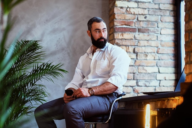 Bebaarde moderne man met smartphone in een kamer met loft interieur.