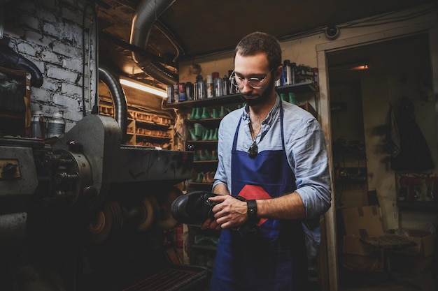 Bebaarde schoenmaker in glazen maakt een nieuw paar schoenen met behulp van een speciale machine.