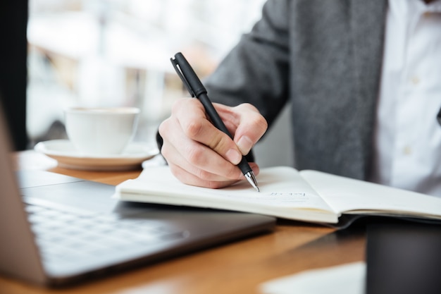 Bebouwd beeld van zakenmanzitting door de lijst in koffie met laptop computer en het schrijven van iets