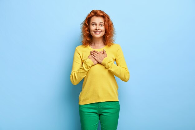 Bedankt voor je steun. Prachtige roodharige vrouw voelt zich aangeraakt en drukt dankbaar de handen op de borst, waardeert hulp