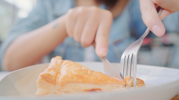 Bedrijfs freelance Aziatische vrouw die brood eet en warme kop van koffie drinkt terwijl het zitten op lijst in koffie.