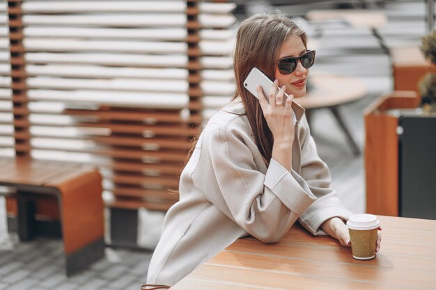 Bedrijfs vrouw in een koffie die coffe, gebruikend telefoon drinkt