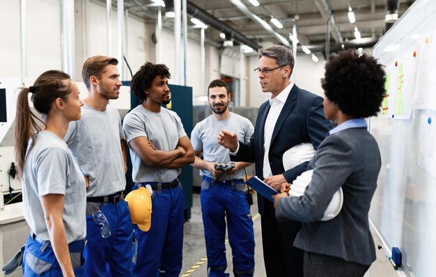 Bedrijfsmanager in gesprek met een groep handarbeiders tijdens een personeelsvergadering in een fabriek