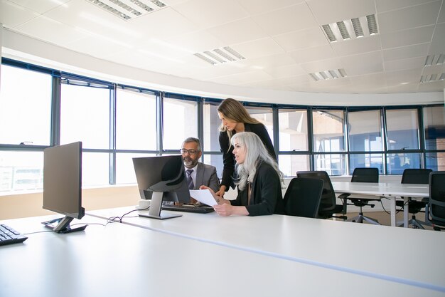 Bedrijfsmanagers verzamelen zich in de vergaderruimte, bekijken samen de projectpresentatie op een computermonitor en houden een papieren rapport vast. Zakelijke communicatie of teamwerk concept