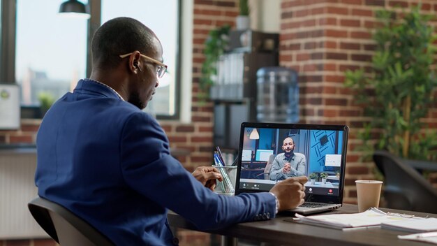 Bedrijfsmedewerker die een externe videogesprekvergadering bijwoont met een man op een laptop, die een gesprek voert op de webcam. Praten met manager over online teleconferentiegesprek, internettelewerkcommunicatie.