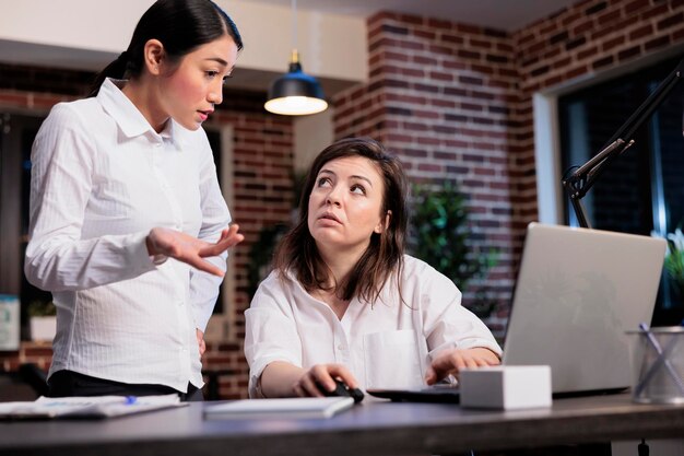 Bedrijfsmedewerkers in kantoorwerkruimte die discussiëren over de marketingstrategie van het opstartproject. Multi-etnische bedrijfsmedewerkers die managementgrafieken analyseren tijdens het gebruik van een laptop.