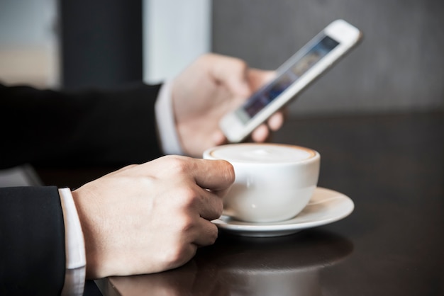 Bedrijfsmens die mobiele telefoon met behulp van terwijl het drinken van koffie in koffiewinkel