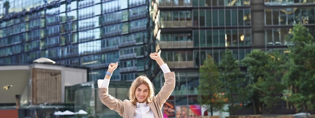 Gratis foto bedrijfsvrouw die haar overwinning buiten op straat viert. gelukkige zakenvrouw die de handen opsteekt en