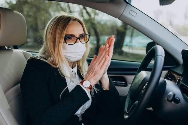 Bedrijfsvrouw in de zitting van het beschermingsmasker in een auto die antiseptisch gebruiken