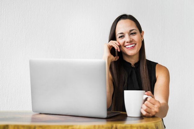 Bedrijfsvrouw met een kop van koffie die bij de telefoon spreekt