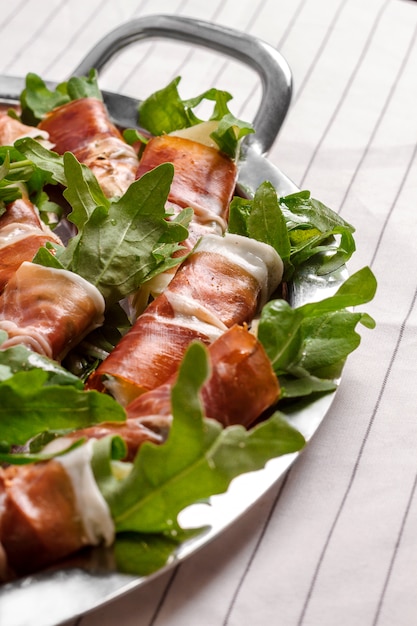 Beeld van baconbroodjes met rucola op witte muur.