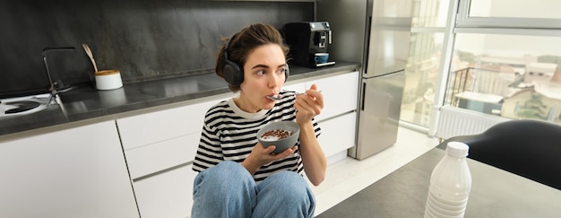 Beeld van een stijlvolle moderne vrouwelijke student die granen eet met melk voor het ontbijt met een kom en een lepel vast