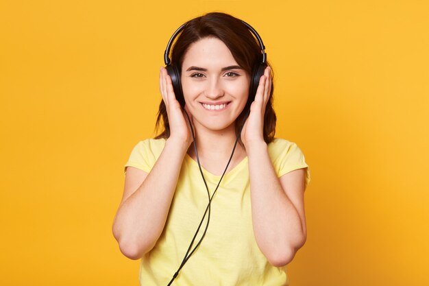 Beeld van jonge gelukkige vrouw die met hoofdtelefoons aan muziek luistert die over geel wordt geïsoleerd