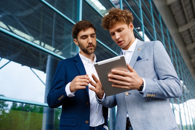 Beeld van twee jonge zakenlieden die op post spreken en tablet houden