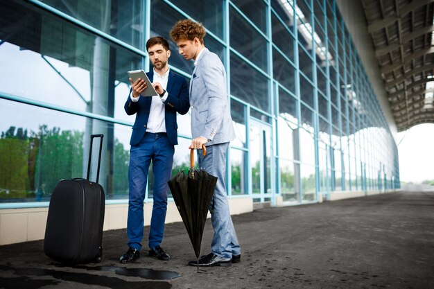 Beeld van twee jonge zakenlieden die op terminal spreken en tablet houden