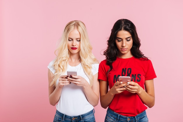 Beeld van twee vrij geconcentreerde vrouwen die haar smartphones over roze gebruiken