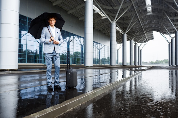 Beeld van zekere jonge redhaired zakenman die zwarte paraplu in regen houden bij luchthaven