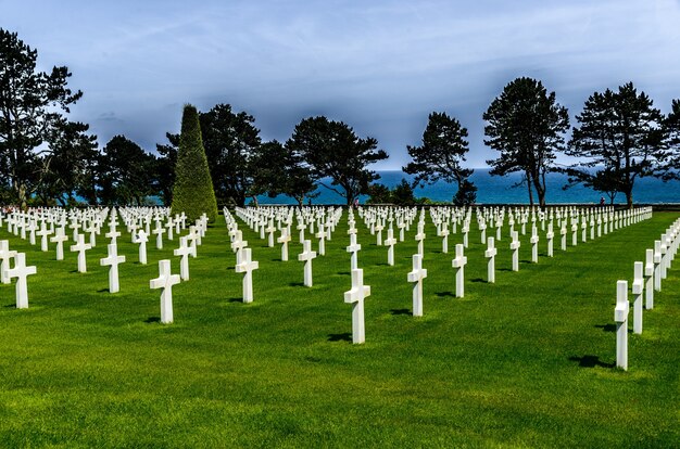 Begraafplaats met witte stenen kruisen omgeven door groene bomen onder de bewolkte hemel